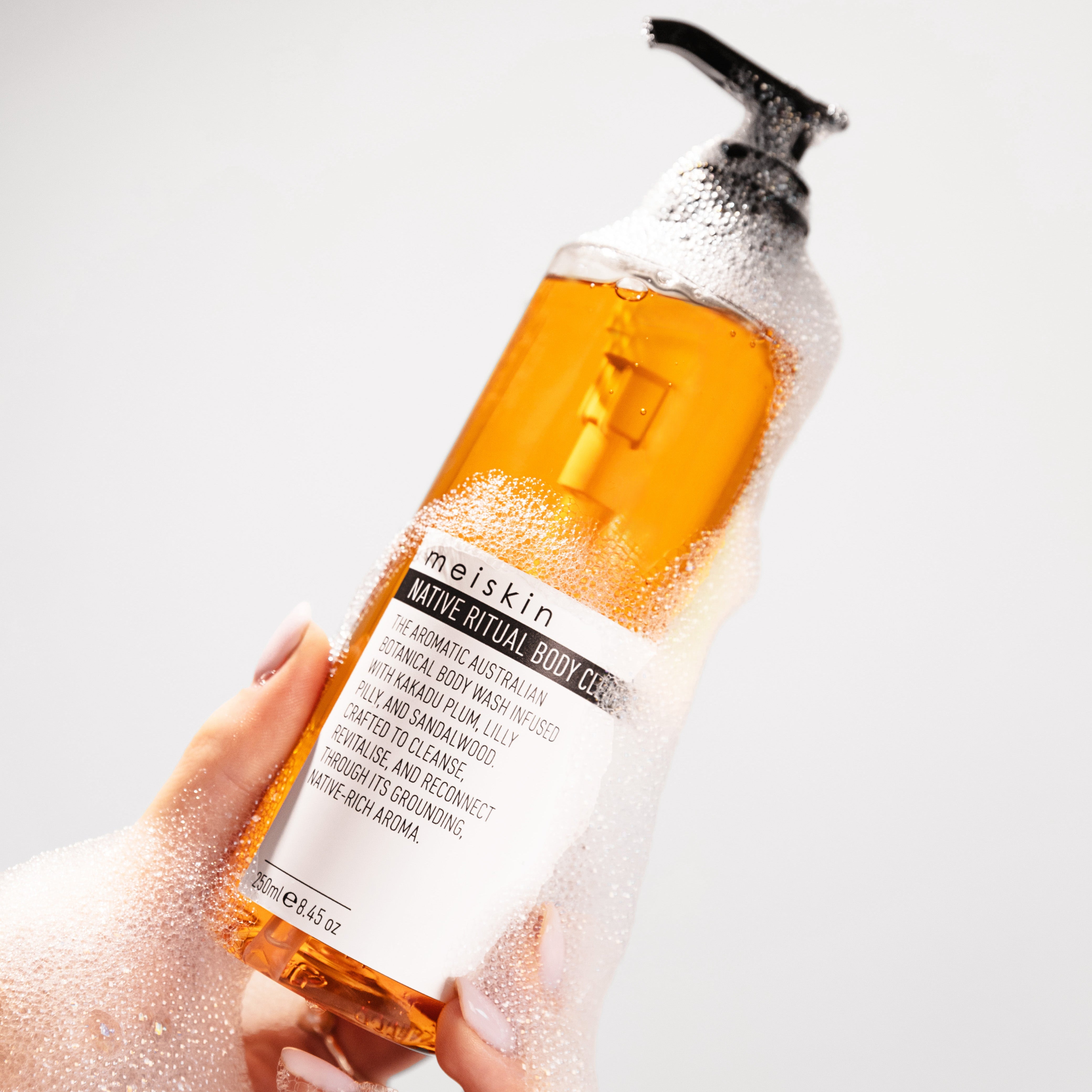 Hand holding a bottle of Meishkin Native Ritual Body Wash with a pump on a white background