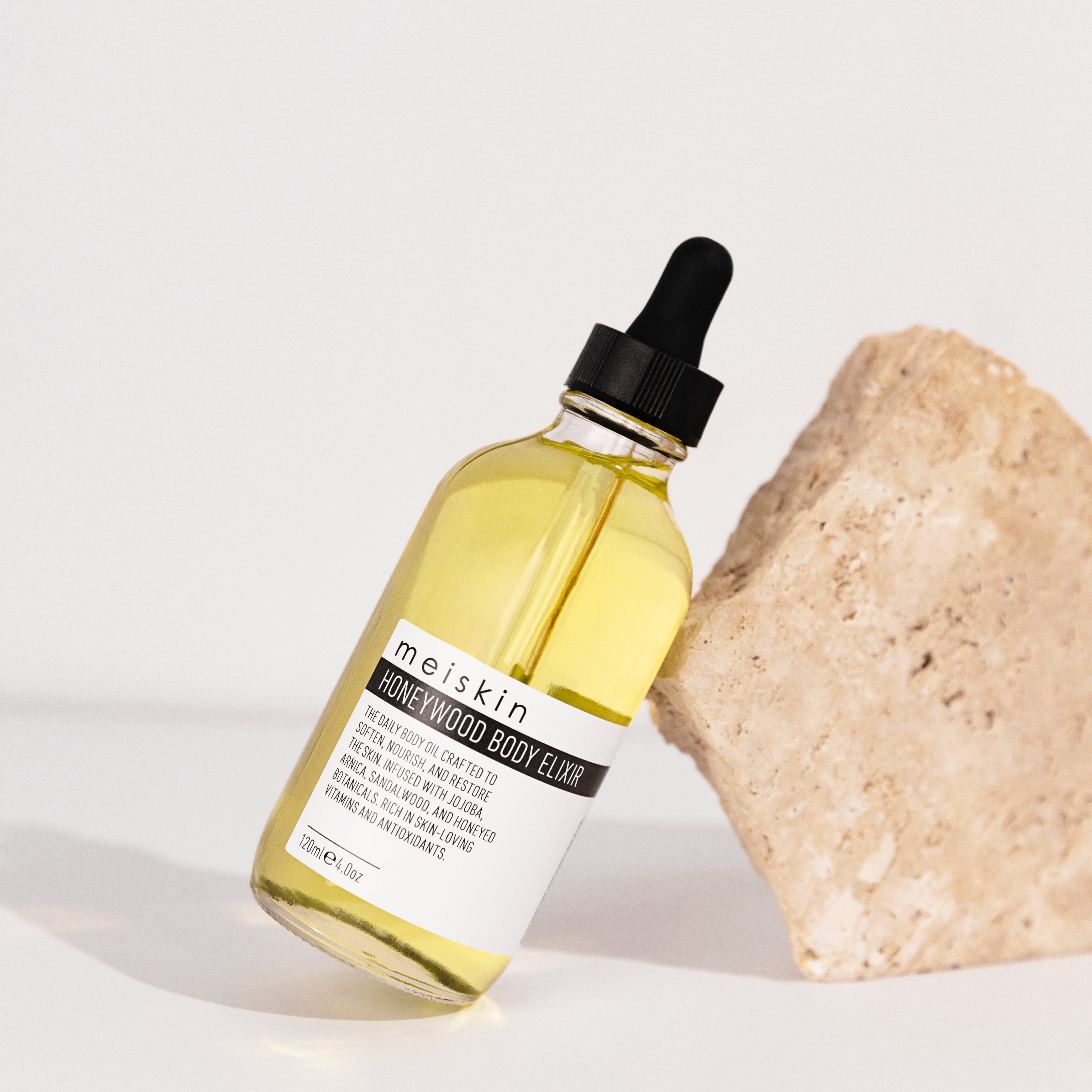 Bottle of meiskin body oil with a dropper next to a stone on a white background