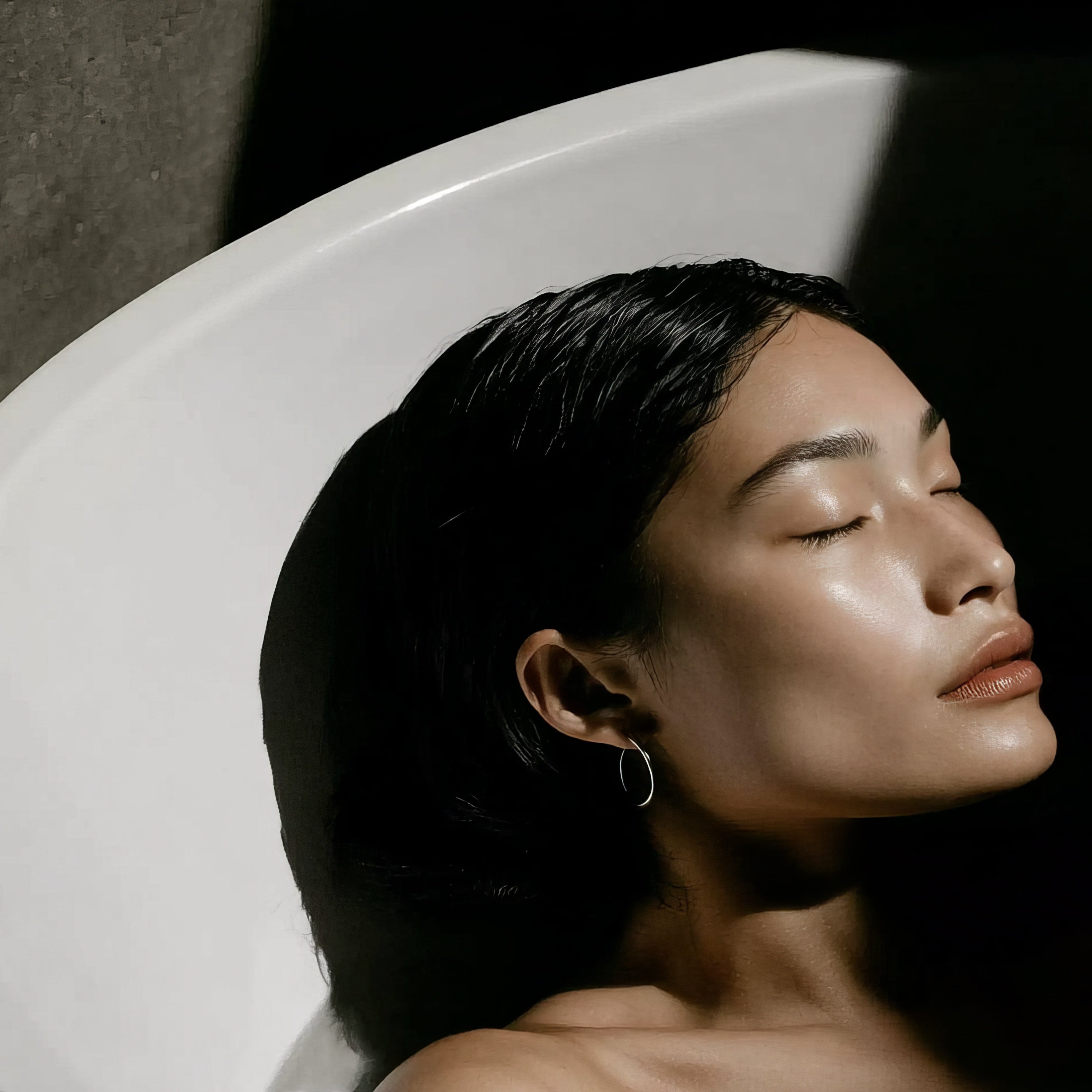 Woman with eyes closed leaning against a white wall.